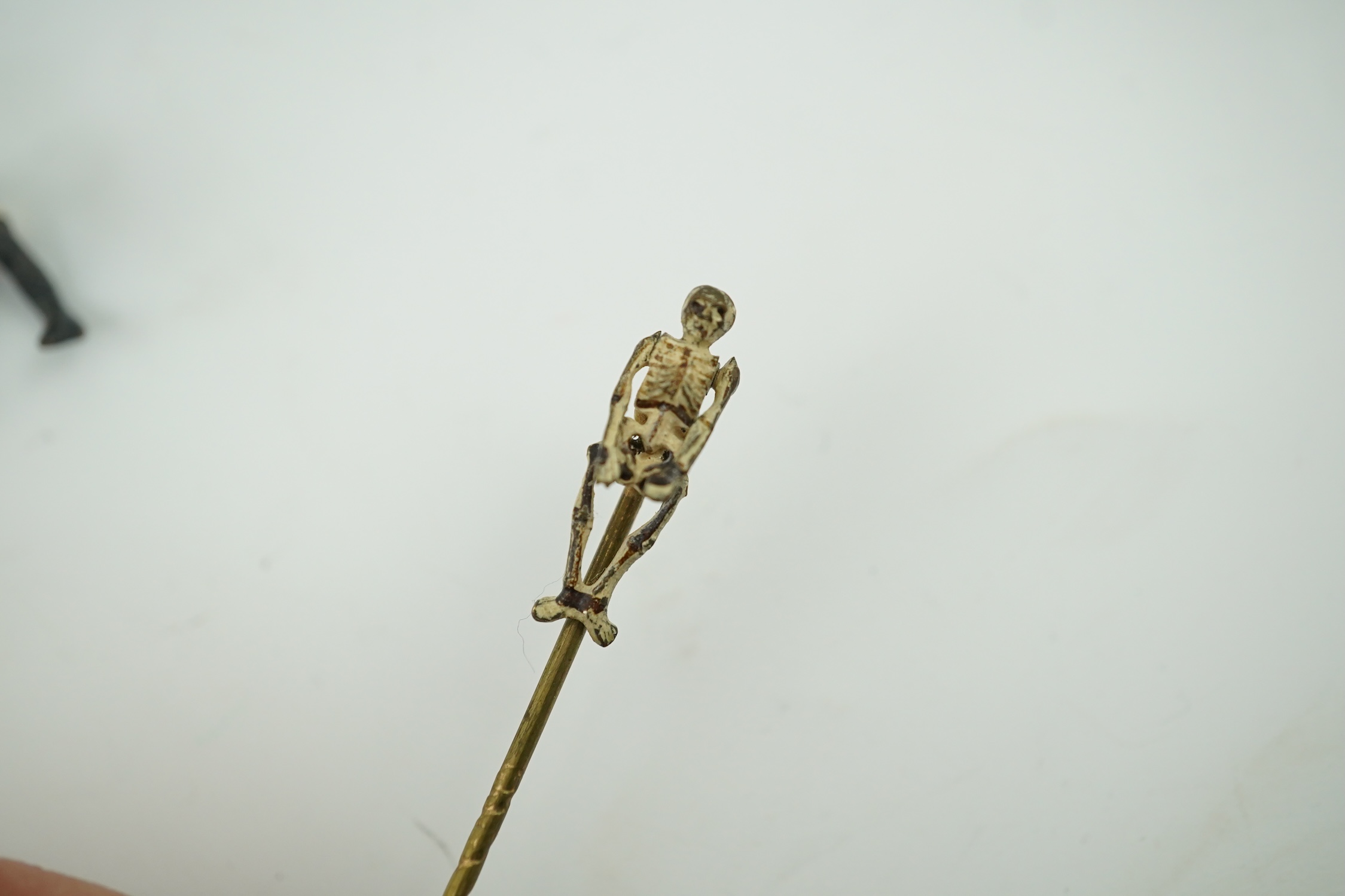 Four novelty miniature cold painted bronzes; black boy with cradle, black baby, cat and pig and a similar articulated arm skeleton stickpin,7cm long. Condition - some chipping to paint